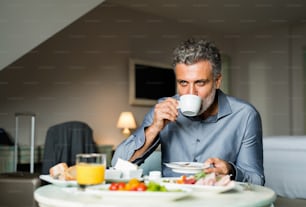 Hombre de negocios maduro y guapo desayunando en una habitación de hotel, bebiendo café.
