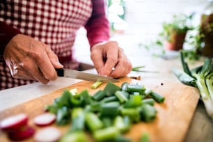 Unrecognizable senior man preparing food in the kitchen. An old man chopping vegetables.