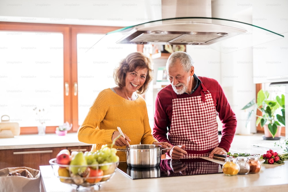 Casal de idosos preparando comida na cozinha. Um velho e uma mulher dentro da casa.
