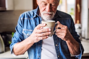 Älterer Mann in der Küche. Ein alter Mann im Haus, der eine Tasse Kaffee in der Hand hält.