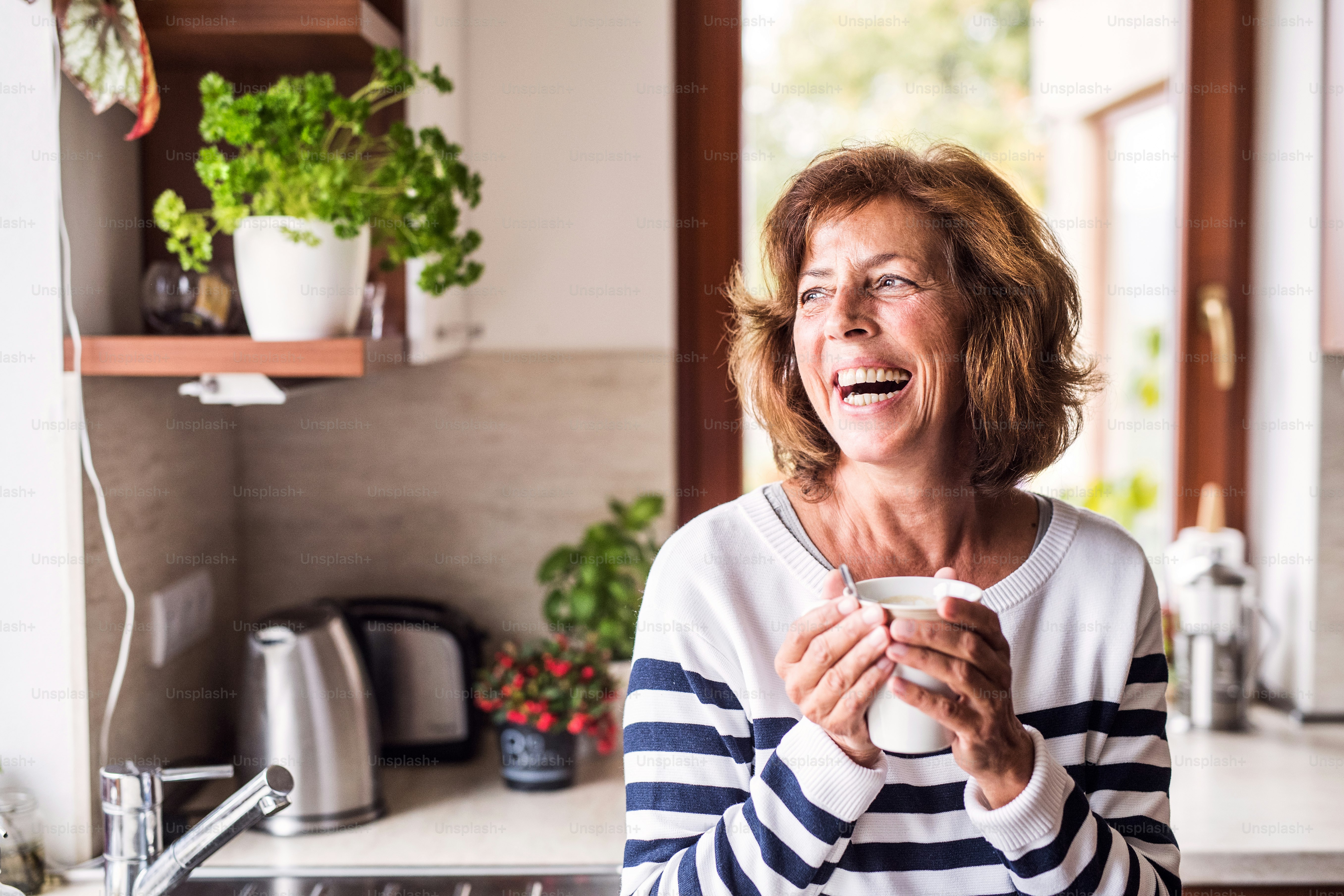 Femme âgée dans la cuisine. Une vieille femme à l’intérieur de la maison, tenant une tasse de café.