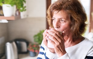 Femme âgée dans la cuisine. Une vieille femme à l’intérieur de la maison, tenant et buvant une tasse de café.