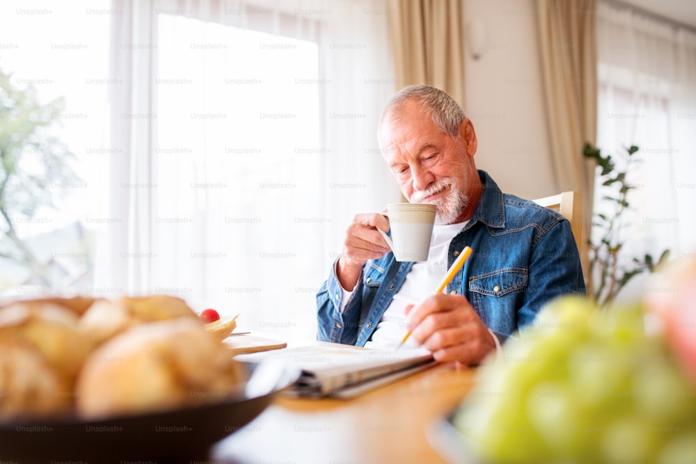 Uomo anziano che fa colazione e fa parole crociate a casa. Un vecchio seduto al tavolo, rilassante.