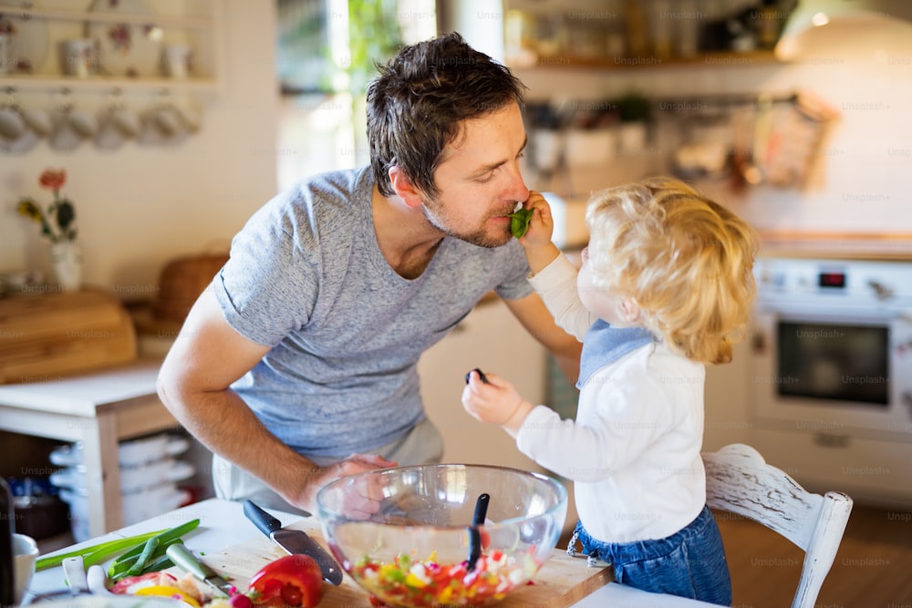 Padre joven con un niño pequeño cocinando. Un hombre con su hijo haciendo ensalada de verduras.