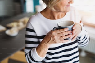 Donna anziana irriconoscibile in cucina. Una donna anziana all'interno della casa, con in mano una tazza di caffè.