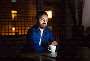 A handsome man working on a laptop at home or in an office at night, with a cup of coffee.