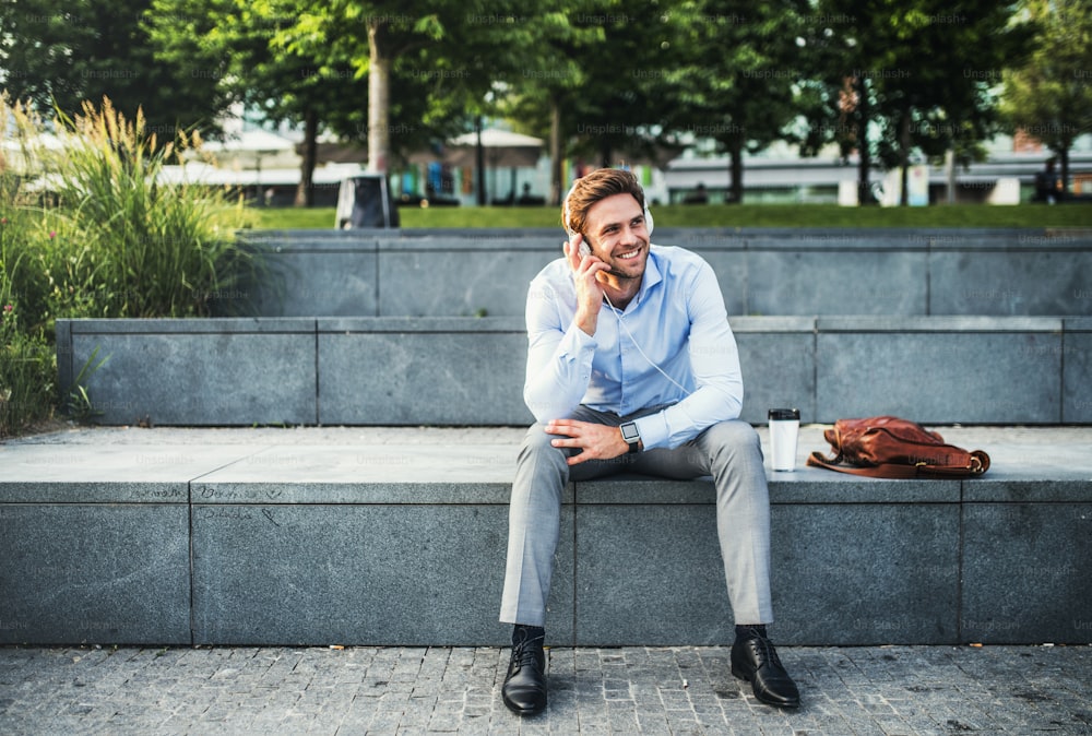 A businessman with smartwatch and headphones, sitting outdoors on concrete stairs.