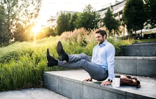 Un uomo d'affari felice all'aperto su scale di cemento al tramonto, alzata in posizione L-seduta.