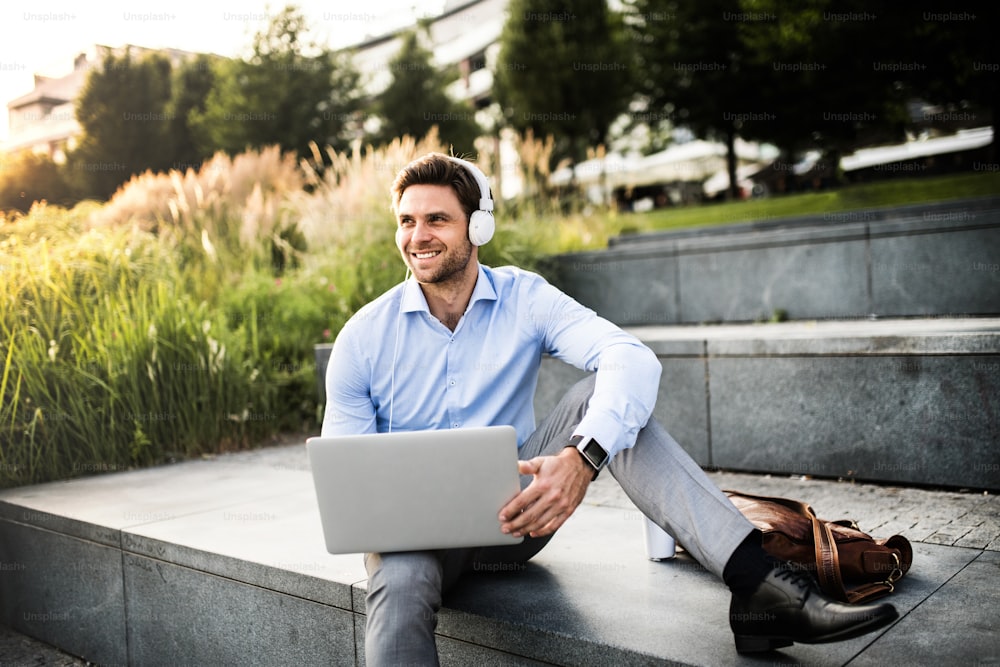 A businessman with smartwatch and headphones, sitting outdoors on concrete stairs.