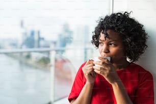 A close-up of a woman standing by the window drinking coffee. Copy space.