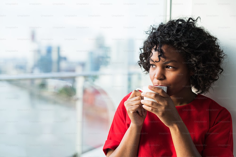 A close-up of a woman standing by the window drinking coffee. Copy space.