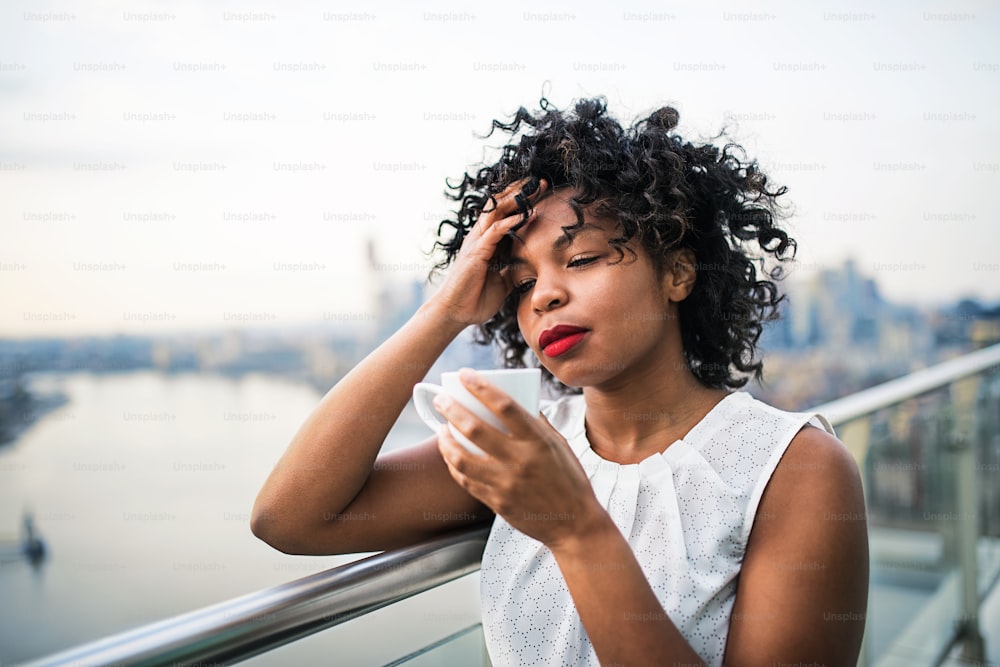 Un ritratto ravvicinato di una donna nera in piedi su una terrazza, bevendo caffè. Copia spazio.