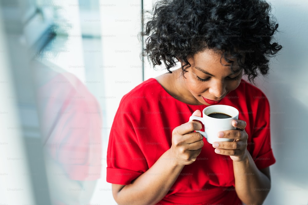 Eine Nahaufnahme einer Frau, die am Fenster steht und eine Tasse Kaffee in der Hand hält und daran riecht. Speicherplatz kopieren.