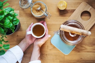 Una composición de manos femeninas sosteniendo taza de té, tetera y azúcar sobre una mesa de madera. Una vista superior.