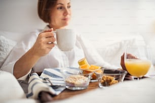 한 젊은 여성이 침대에 누워 아침에 실내에서 커피와 아침 식사를 하고 있다.