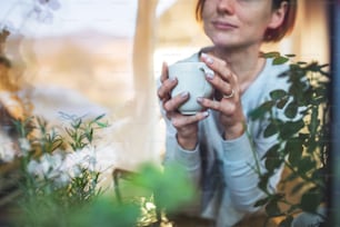 A midsection of young woman with cup of coffee looking out of a window. Shot through glass. A copy space.