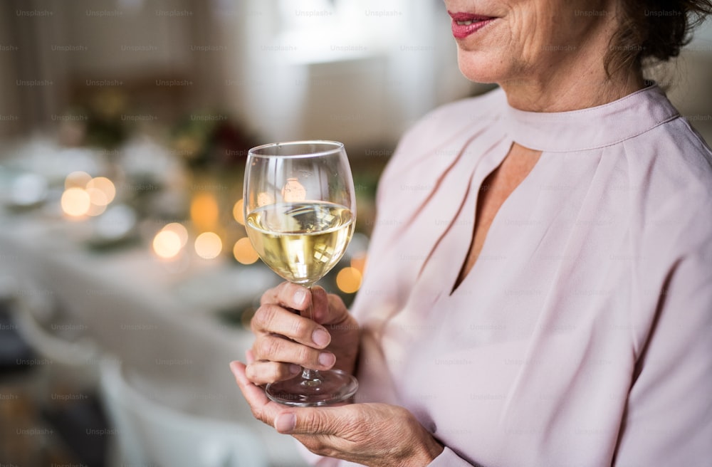 Una parte centrale di una donna anziana in piedi in una stanza allestita per una festa, con in mano un bicchiere di vino. Copia spazio.