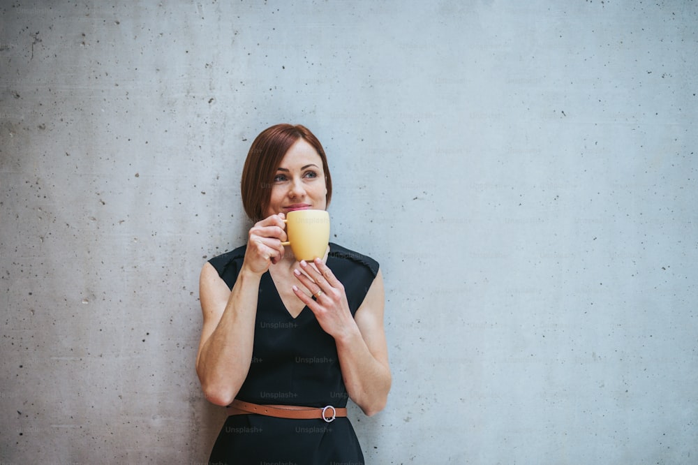 Ein Porträt einer jungen fröhlichen Geschäftsfrau, die im Büro steht und eine Tasse Kaffee in der Hand hält.