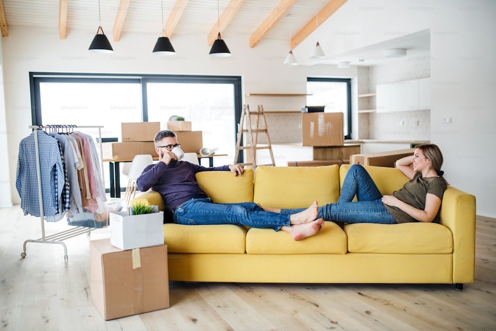 Um jovem casal com xícara de café sentado no sofá, movendo-se em nova casa.