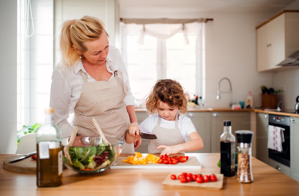 Un ritratto di bambina con la nonna in una cucina a casa, preparando insalata di verdure.