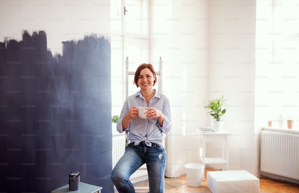 A portrait of young creative woman with a cup of coffee painting wall black. A startup of small business.