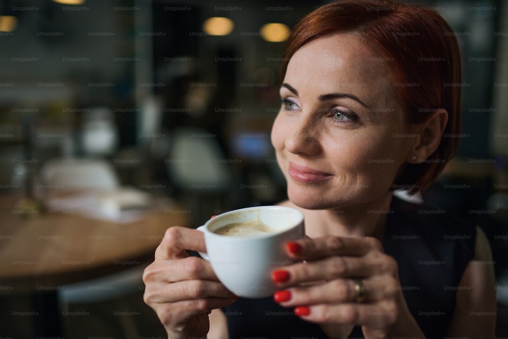 Porträt einer attraktiven Frau, die in einem Café sitzt und eine Tasse Kaffee in der Hand hält.