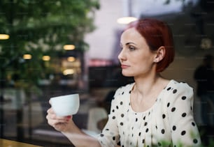 Un portrait de femme avec un café assis à la table dans un café, utilisant un ordinateur portable. Tiré à travers le verre.