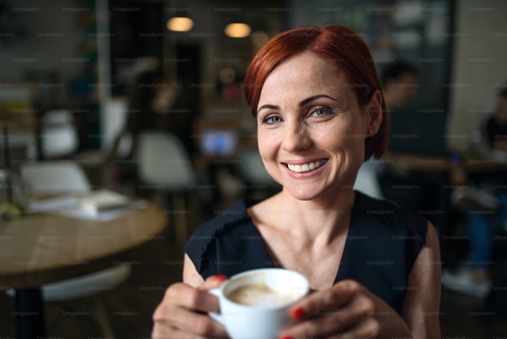 Porträt einer attraktiven Frau, die in einem Café sitzt und eine Tasse Kaffee in der Hand hält.