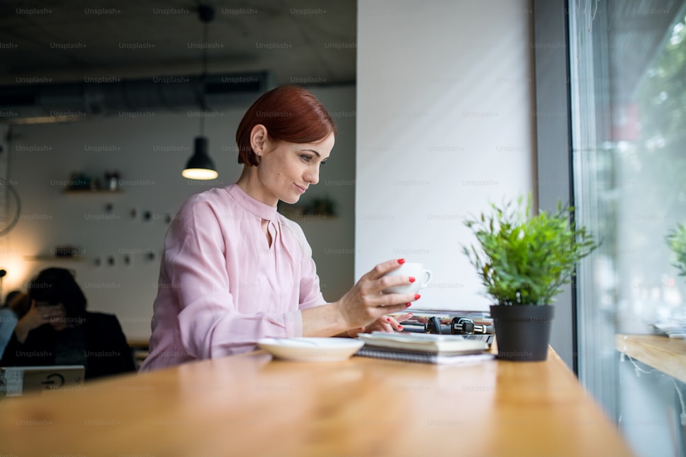 A portrait of attractive woman with coffee sitting at the table in a cafe, working.