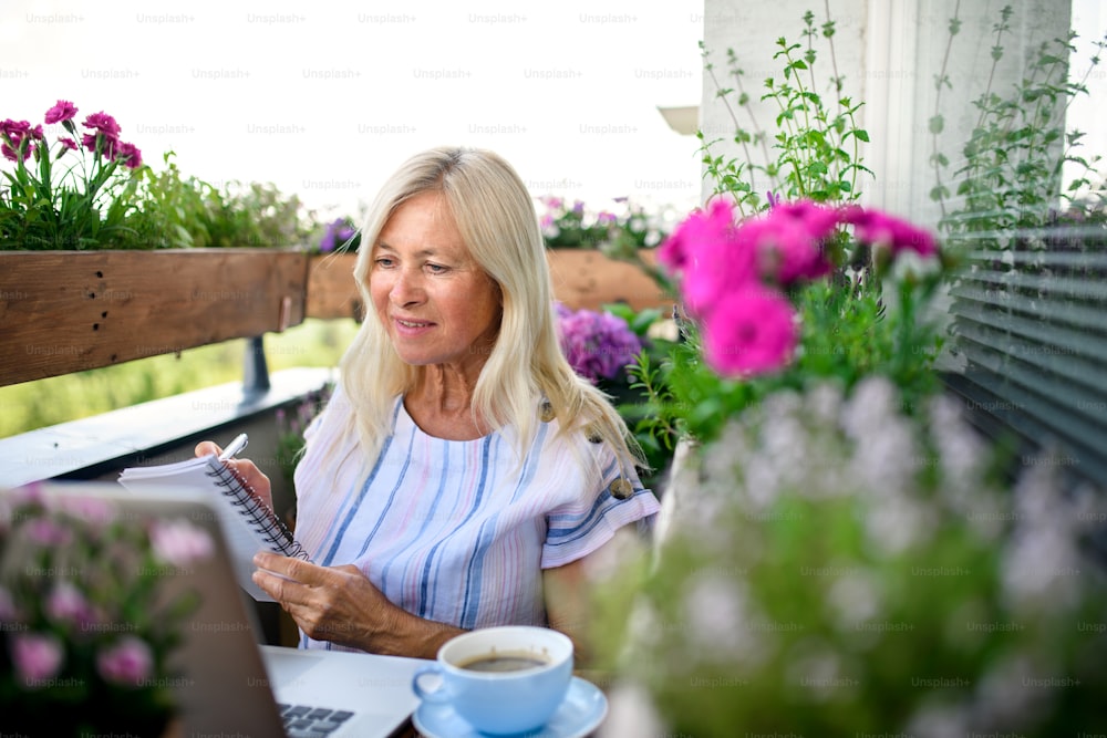 Active senior woman with laptop working on balcony, home office concept.