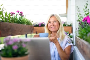 Aktive Seniorin mit Laptop und Kaffee, Arbeit auf Balkon, Home-Office-Konzept.