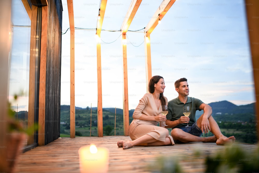 Young couple with wine sitting outdoors, weekend away in container house in countryside.