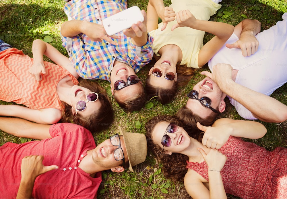 Group of young people having fun in park, lying on the grass and taking selfie