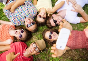 Group of young people having fun in park, lying on the grass and taking selfie