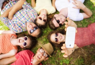Gruppo di giovani che si divertono nel parco, sdraiati sull'erba e scattano selfie