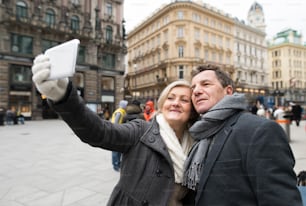 Beau couple de personnes âgées en vêtements d’hiver lors d’une promenade dans le centre historique de la ville de Vienne, en Autriche. Femme prenant un selfie d’eux avec un téléphone intelligent.