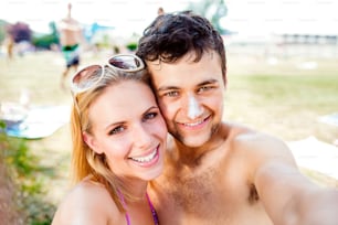 Young couple sunbathing, taking selfie. Sunscreen on the nose. Summer heat. Woman with sunglasses in bikini.