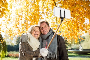 Belle personne âgée prenant selfie avec un téléphone intelligent. Journée ensoleillée dans le parc d’automne.