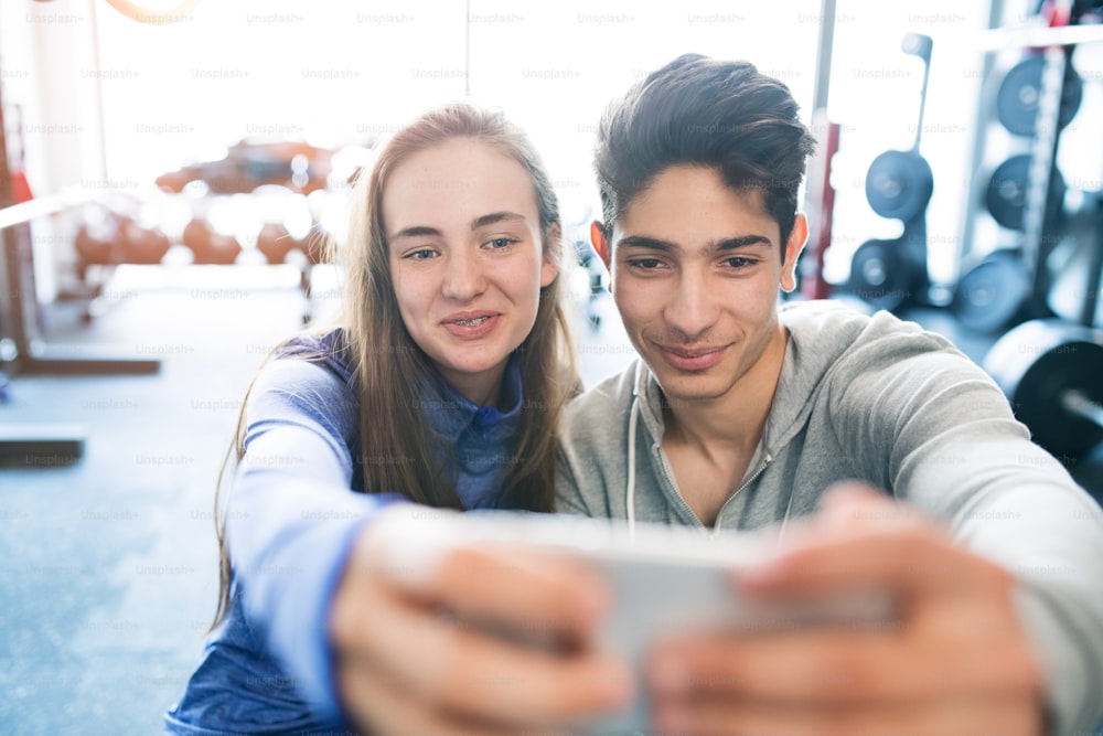 Schönes junges fittes Paar im modernen Fitnessstudio mit Smartphone, Selfie machend.