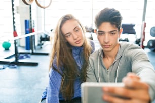 Beautiful young fit couple in modern  gym with smart phone, taking selfie.