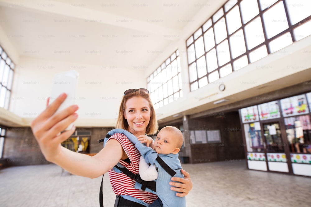 Young mother with smartphone and baby travelling. A beautiful woman and her son inside the station building.