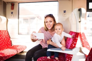 아기와 함께 기차로 여행하는 젊은 엄마. 아름다운 여인과 그녀의 아들의 철도 여행. 스마트폰으로 셀카를 찍는 여자.