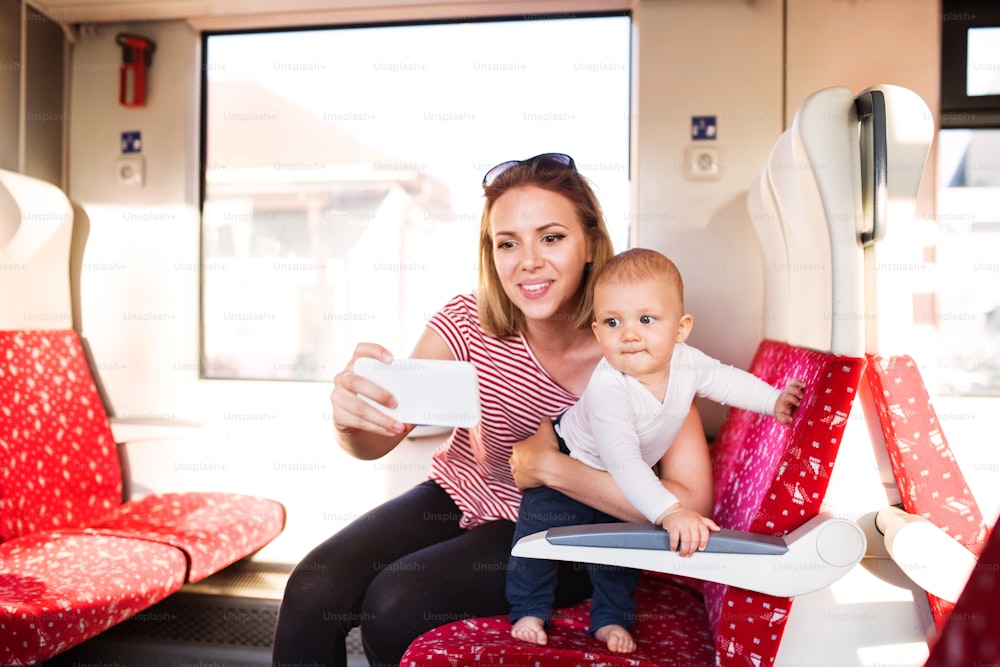아기와 함께 기차로 여행하는 젊은 엄마. 아름다운 여인과 그녀의 아들의 철도 여행. 스마트폰으로 셀카를 찍는 여자.