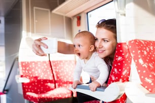 Young mother travelling with baby boy by train. Railway journey of a beautiful woman and her son. A woman taking selfie with a smartphone.