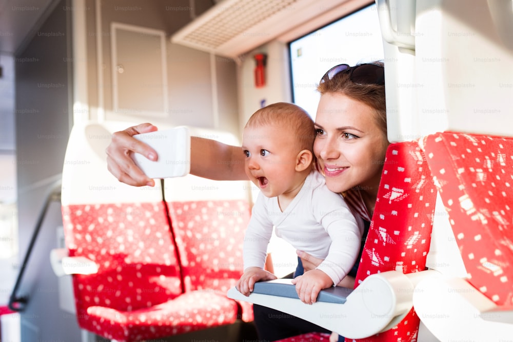 Madre joven que viaja con un bebé en tren. Viaje en tren de una hermosa mujer y su hijo. Una mujer tomándose selfie con un teléfono inteligente.