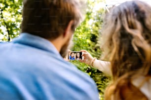 Schönes junges Paar mit Smartphone, das Selfie macht. Sonniger Frühlingstag. Rückansicht. Aufschließen.