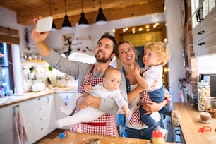 Linda família jovem fazendo biscoitos em casa. Pai, mãe. menino e bebê tirando selfie com um smartphone.