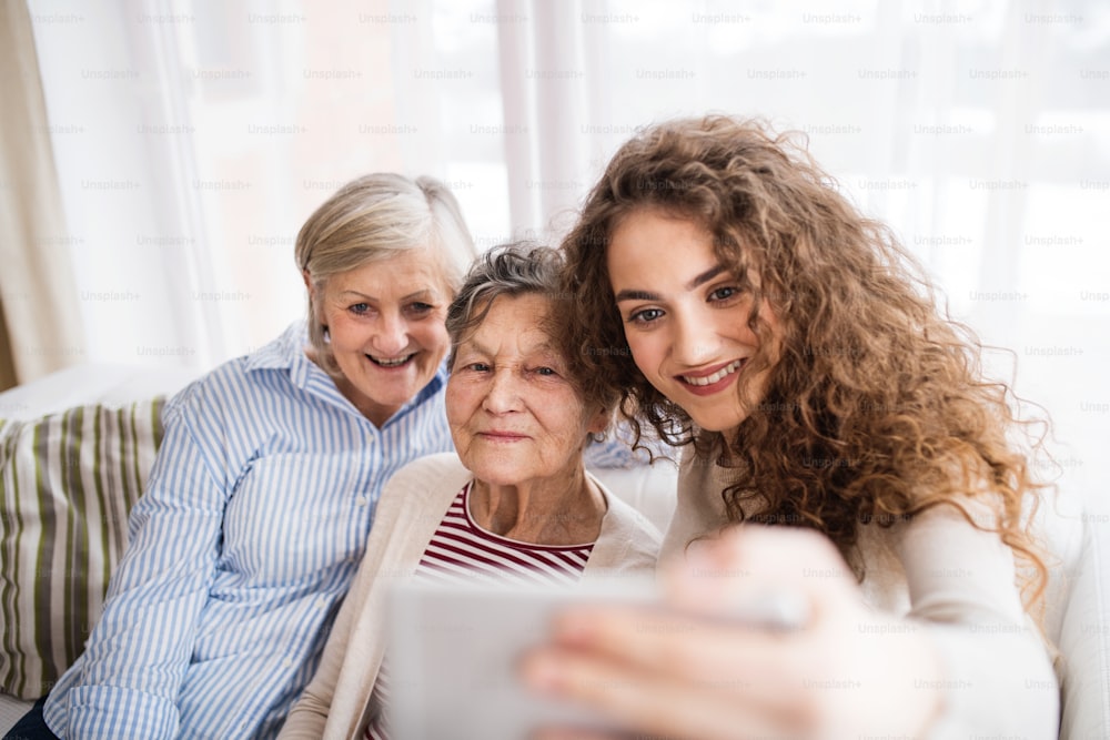 Una ragazza adolescente, sua madre e sua nonna con lo smartphone a casa, che scattano selfie. Concetto di famiglia e generazioni.