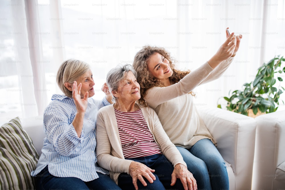 Una ragazza adolescente, sua madre e sua nonna con lo smartphone a casa, che scattano selfie. Concetto di famiglia e generazioni.