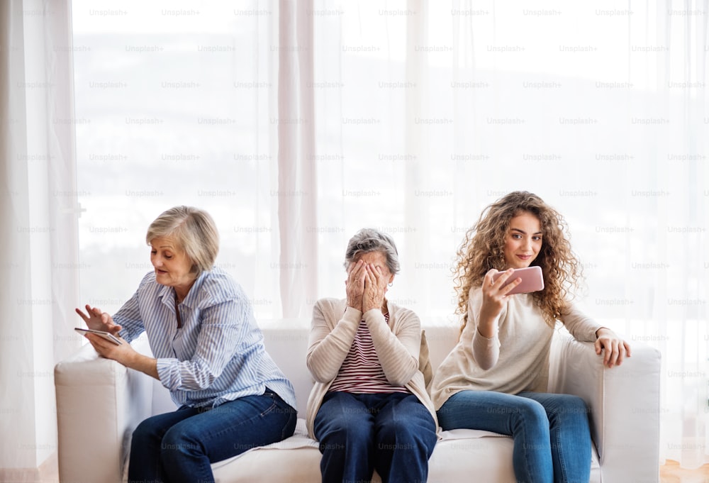 Una ragazza adolescente, sua madre e sua nonna con lo smartphone a casa. Concetto di famiglia e generazioni.